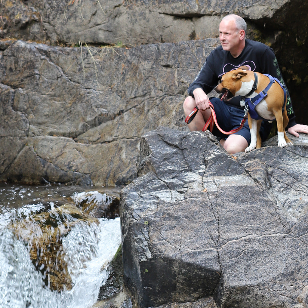 Photo of Scott Hampton on high rocks next to a waterfall, accompanied by his dog, "Massimo".