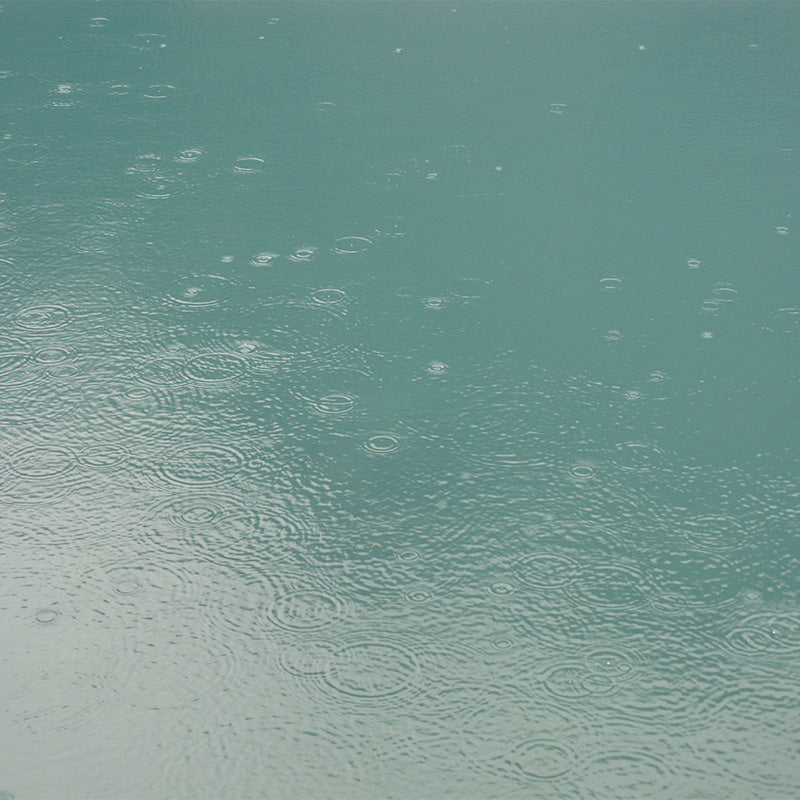 Nature's texture as inspiration: Rain drops form puddle rings in a pale teal glacial lake.