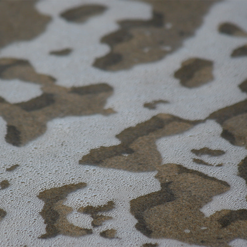 Nature's texture as inspiration: Lacey patterns of sea foam appear floating in crystal clear water, casting subtle shadows on the sand beneath.